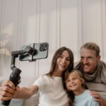A mother, daughter and father recording themselves smiling on a couch, using the DJI Osmo Mobile 8.