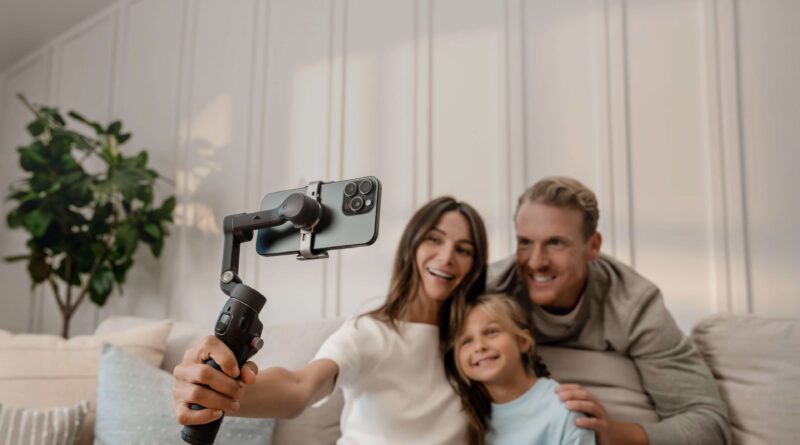 A mother, daughter and father recording themselves smiling on a couch, using the DJI Osmo Mobile 8.